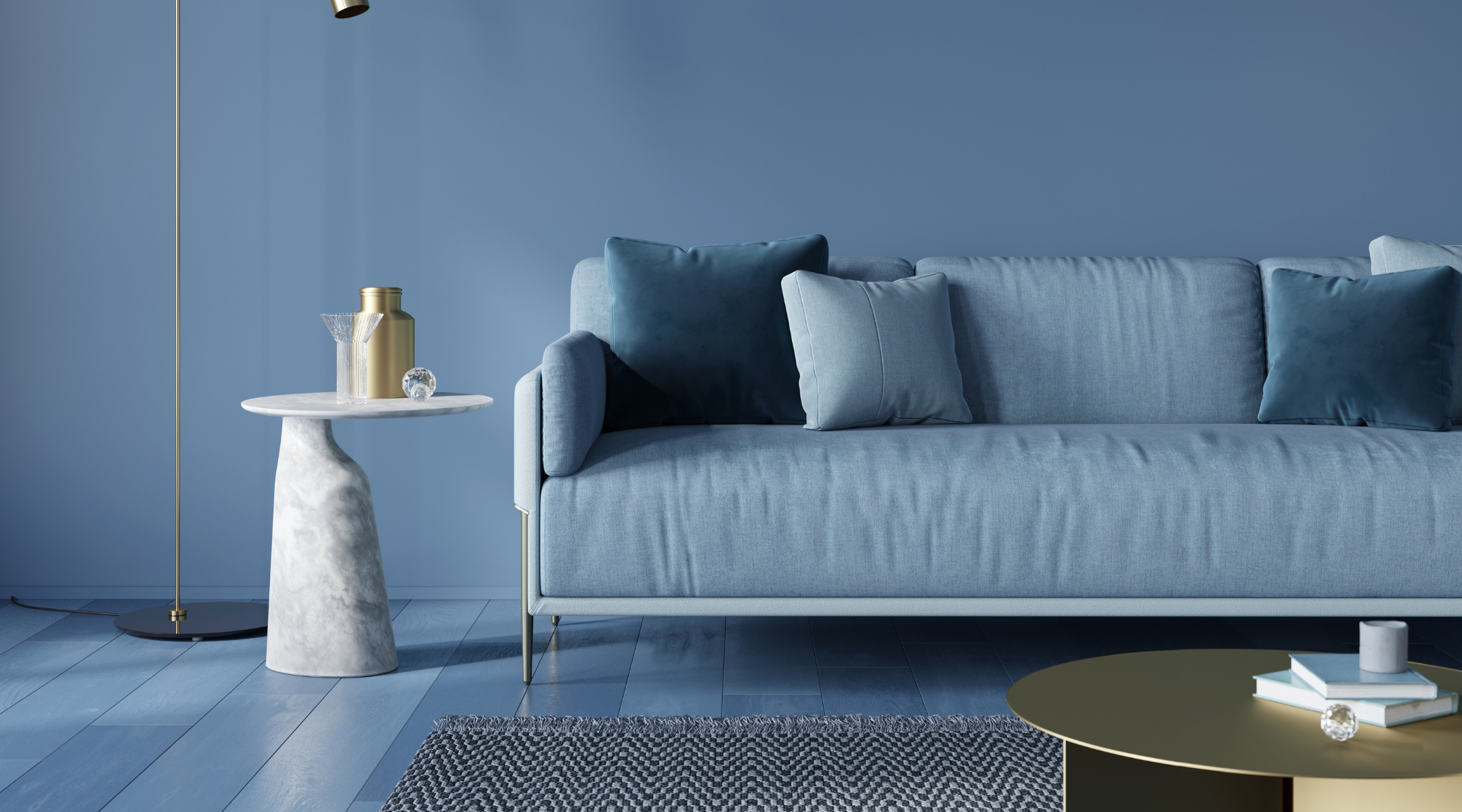 Blaues Sofa vor blauer Wand mit grauem Beistelltisch aus Marmor und goldenem Couchtisch